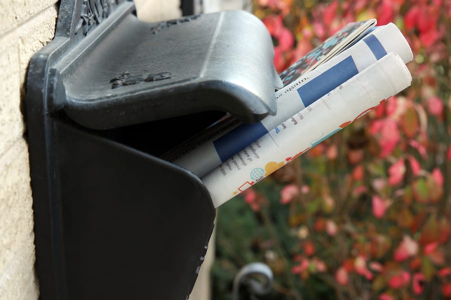 A Pile Of Newspapers On A Mail Box